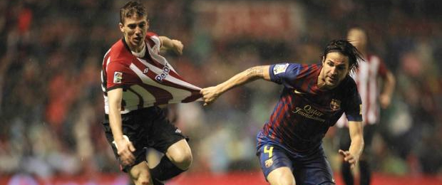 Iker Muniain y Cesc Fábregas pugnan por un balón